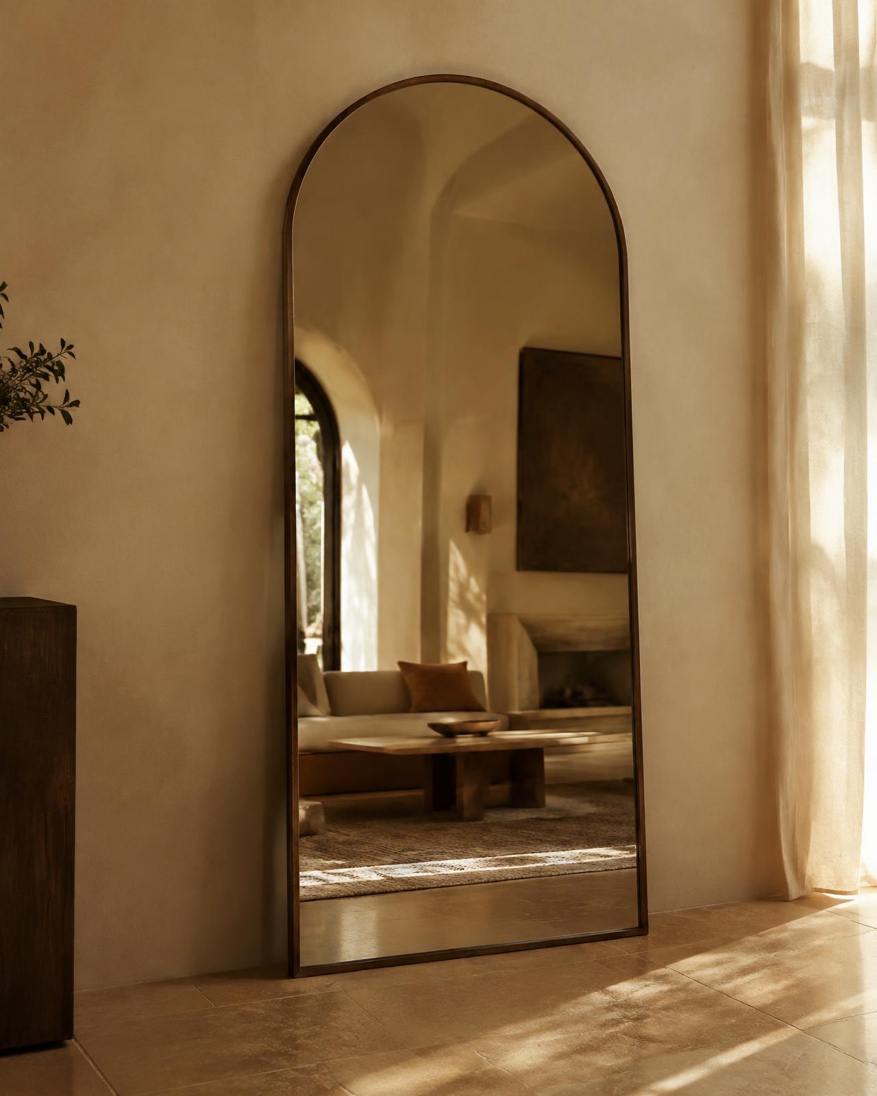 Grand miroir arche en bois foncé contre un mur en plâtre ivoire